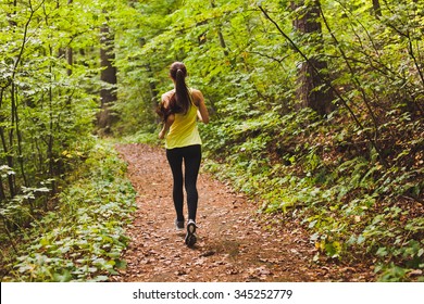 Young athletic sporty girl with long hair in green sleeveless shirt training in green forest during summer autumn season with lots of leaves fallen on forest path. Back view with copy space - Powered by Shutterstock