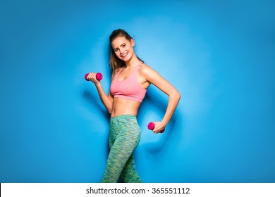 young athletic woman in colored equipment lifting weights on blue background