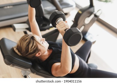Young athletic woman doing bench press using dumbbells in gym - Shutterstock ID 1904011156