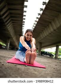 Young Athletic Woman Doing Seated Forward Bend Stretching. Fit Girl Touching Toes Smiling Exercising Outdoors In Parking Lot. 