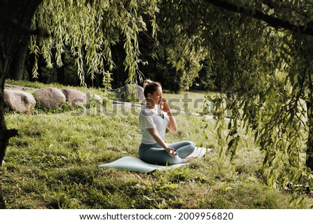 Young athletic woman during yoga class performing Pranayama breathing practice, exercise with alternate nostrils in the morning, outdoors. Girl meditating under a tree in the park, healthy lifestyle.
