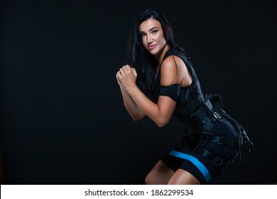 A young athletic woman in an EMS suit exercising on an isolated black background. EMS training. Electro muscular stimulation machine.