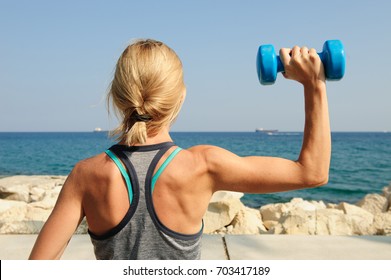 Young athletic woman exercising outdoors: overhead press for upper body strength