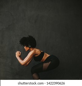 Young athletic woman exercising squats against a grey wall. Fit woman doing squats outdoors in morning.