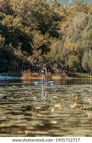 Young athletic woman SUP stand up paddle board on a river overgrown with grass in Montenegro