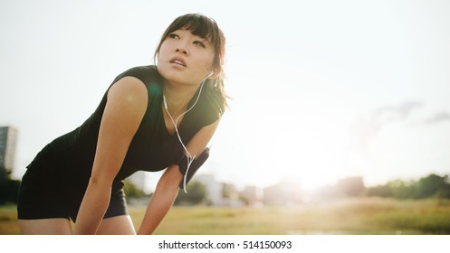 Young athletic woman taking a break from training. Chinese female standing with hands on her knees and looking away in morning. - Powered by Shutterstock