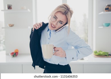 Young Attractive Adorable Smiling Blonde Woman Office Executive Worker Wearing Spectacles In Hurry Early In The Morning Talking On The Phone Putting Dark Blue Jacket On Having A Drink In Kitchen