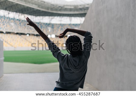 Young attractive african american female in gray hoodie dancing alone at empty stadium