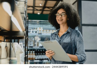 Young attractive african barista bartender waitress checking the quality of goods, doing inventory taking notes holding a folder clipboard in coffee shop cafeteria - Powered by Shutterstock