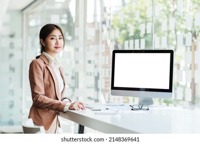 Young Attractive Asian Business Woman Looking At Camera, Blank White Screen Monitor For Mock Up Display Your Ads.