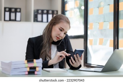 Young attractive Asian business woman with messy desk in office,  sitting at the desk, working at contemporary office and documents. make a mobile phone call - Shutterstock ID 2232907043