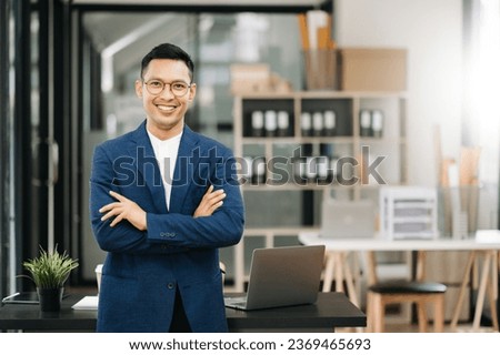 Young attractive Asian Businessman smiling thinking planning writing in notebook, tablet and laptop  looking at camera at office 
