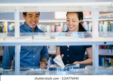 A young and attractive Asian Chinese couple browse books in a library or book store during a date. They are middle-aged, confident and well-dressed.