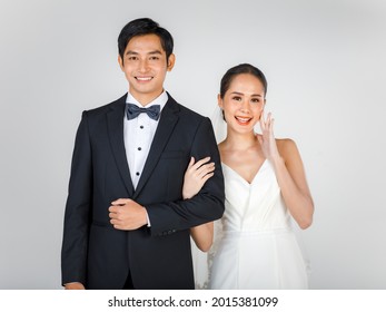 Young Attractive Asian Couple, Bride And Groom, Woman Wearing White Wedding Dress. Man Wearing Black Tuxedo, Standing Arm In Arm Together. Concept For Pre Wedding Photography.