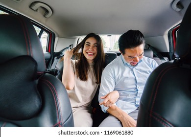 A Young And Attractive Asian Couple Sit Together In The Backseat Of A Car As They Are Driven To Their Destination. They Booked Their Ride On A Ride Hailing App. 