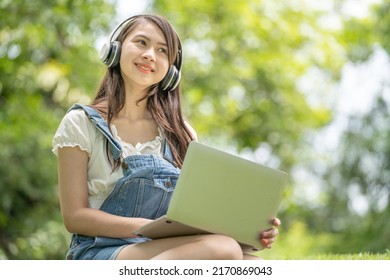 Young Attractive Asian Female Employee Wear Earphone Listen To Digital Online Course Development Study Online In The Park