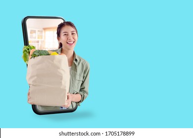 Young Attractive Asian Female Hold Shopping Groceries Bag Happy Smiling On Supermarket Online Store Discount Promotion With Concept Tech On Omnichannel Delivery Service E-commerce Thru Mobile Screen.