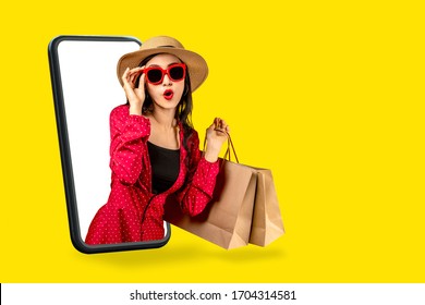 Young attractive asian female holding shopping bag feeling excited, happy and amaze on beauty or fashion online store discount promotion with concept tech on omnichannel e-commerce thru mobile screen. - Shutterstock ID 1704314581