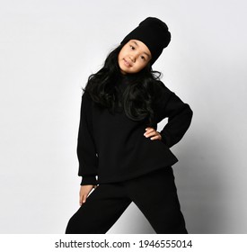 Young Attractive Asian Girl In Dark Ten Years Old In Warm Autumn Or Spring Black Sportswear And A Hat Posing For The Camera, Put Her Hand On Her Waist