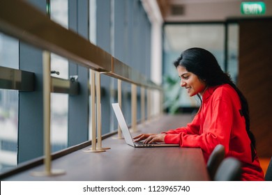 A young and attractive Asian Indian student woman works on her notebook laptop at a wooden desk during the day. She is focused and typing on her notebook; the very image of productivity. - Powered by Shutterstock