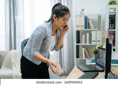 Young Attractive Asian Japanese Female Entrepreneur Talking On Mobile Phone While Standing At Desk In High Key Bright Home Office. Elegant Woman Manager Having Discussion On Mobile Phone In Day Tim