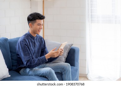 Young Attractive Asian Man Resting Using Browsing Tablet Computer On Sofa At Home, Happy Male Sitting On Couch Relax Reading Digital Gadget At House, Communication And Lifestyle Concept.