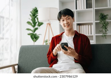 Young attractive Asian man smiling thinking planning writing in notebook, tablet and laptop working from home, looking at camera at home office  - Shutterstock ID 2307986129