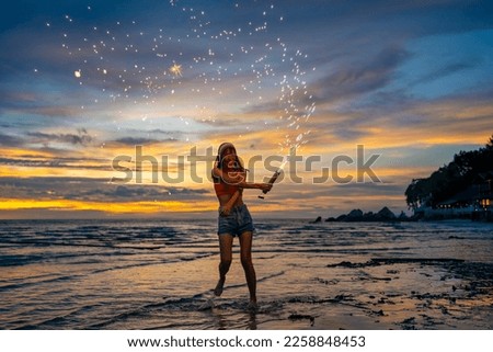 Young attractive Asian woman dancing and playing sparklers firework at tropical island beach in summer night. Happy girl enjoy and fun outdoor lifestyle travel nightlife party on holiday vacation trip