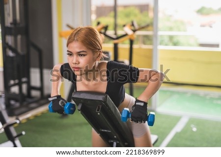 A young and attractive asian woman does chest supported dumbbell rows on an incline bench. Working out back muscles at the gym.