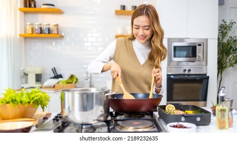 Young Attractive Asian Woman Enjoy Cooking Healthy Food And Pasta In Cooking Pan On Stove In The Kitchen At Home. Happy Female Having Dinner Meeting Party Celebration With Friends On Holiday Vacation.