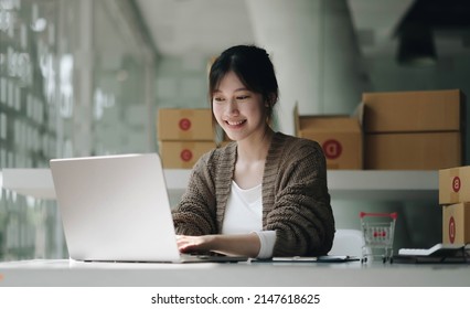 Young Attractive Asian Woman Owner Startup Business Look At Camera Work Happy With Box At Home Prepare Parcel Delivery In Sme Supply Chain, Procurement, Omnichannel Or Coronavirus Quarantine Concept.
