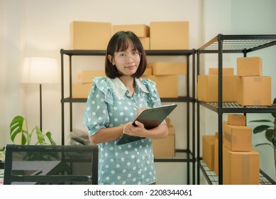 Young Attractive Asian Woman Owner Startup Business Look At Camera Work Happy With Box At Home Prepare Parcel Delivery In Sme Supply Chain, Procurement, Omnichannel Or Coronavirus Quarantine Concept.