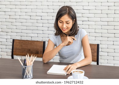 Young Attractive Asian Woman Smiling Thinking Planning Writing Memo In Notebook Working From Home