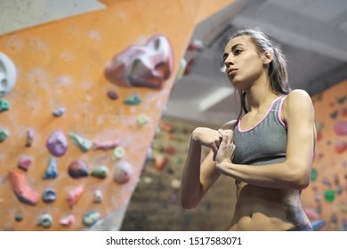 young attractive Athletic woman with muscular naked torso stretching arms before climb in indoor climbing gym. Exercising and training in climbing gym. Concept of strength, sport, healthy lifestyle.