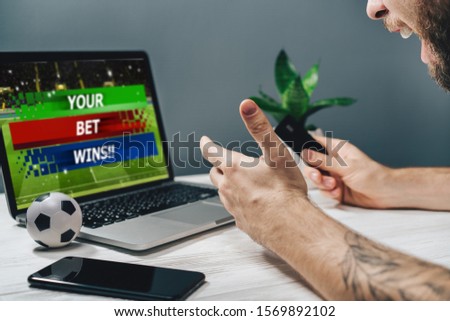 Young attractive bearded man showing sincere excitement about his favorite team victory. Guy being happy winning a bet in online sport gambling application on her mobile phone.