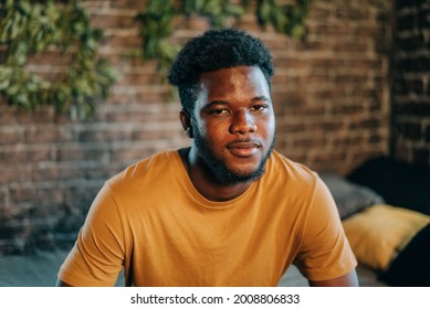 Young Attractive Black Man Portrait With Dark Skin Sitting On The Bed Indoors At Home In The Bedroom Loft Style Design. Real People