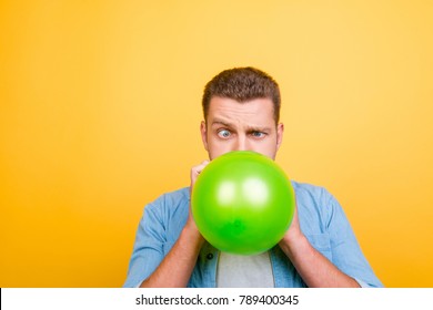 Young attractive blond man tired to blow up balloons new year party, twisted eyes over yellow background