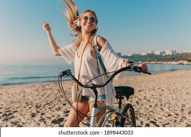 young attractive blond sniling woman walking on beach with bicycle in headphones listening to music in postive happy mood - Powered by Shutterstock