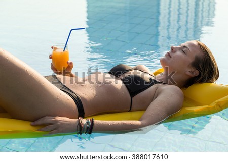 Young, attractive blond woman laying down on a floating matress, holding a glass of an orange juice
