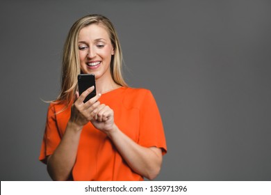 Young attractive blond woman smiling down at her smartphone in her hand.