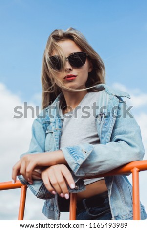 Young attractive blonde in jeans jacket and shorts walking in the city in summer in sunny weather