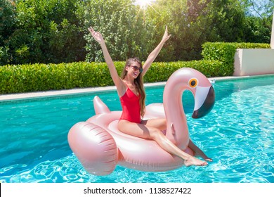 Young, attractive, blonde woman enjoys a hot summer day in the pool with a giant floatable flamingo