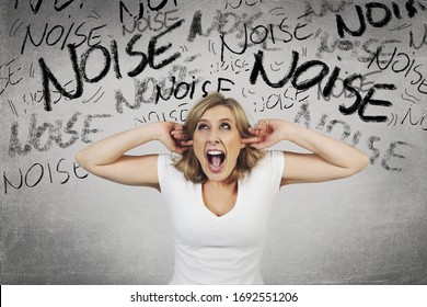 
young and attractive blonde woman pissed off by noise from neighbors blocking ears over gray studio background