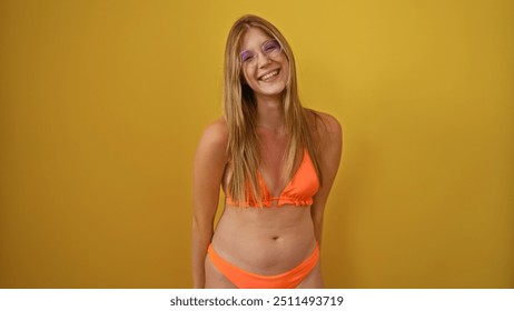 Young attractive blonde woman smiling in an orange bikini over an isolated yellow background - Powered by Shutterstock