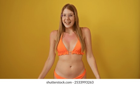 Young, attractive, blonde woman smiling cheerfully in an orange bikini against a vibrant yellow background wall, isolated and beautiful. - Powered by Shutterstock