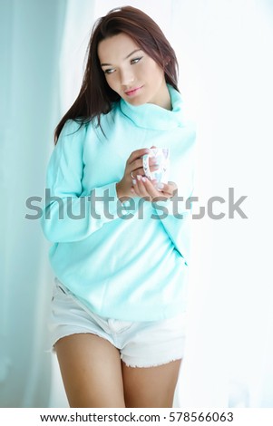 Young attractive brunette with blue eyes in a blue sweater, with a cup of coffee