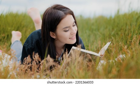 Young Attractive Brunette Caucasian Woman Girl Lying On Grass Pretty Teenage Girlfriend Student Read Interesting Book Educational Literature Novel Bestseller Enjoy History In Textbook Turn Over Pages