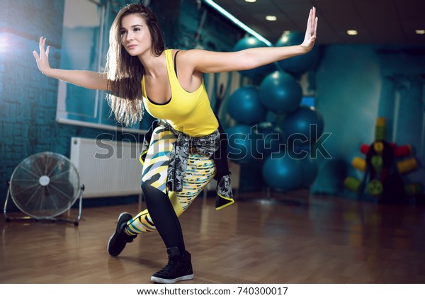 Young attractive brunette woman doing zumba\
dance workout alone in gym. Toned\
image.