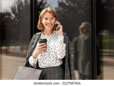 Young Attractive Business Lady Making Call While Walking Along City Street With Take Away Coffee In Hand, Enjoying Pleasant Conversation On Mobile Phone With Client On Her Way To Office In Morning