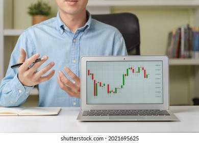 Young attractive businessman or investor teaching in online investing courses on stock market or Cryptocurrency as Bitcoin with trading graphs or tickers on laptop at home. Money investing concept.